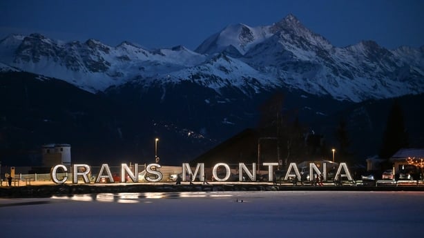 A Crans-Montana sign with snow covered mountains in the distance