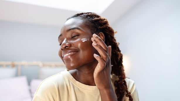 A close-up of a young African American woman applying beauty cream
