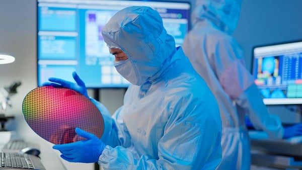 asian male technician in sterile coverall holds wafer that reflects many different colors with gloves and check it at semiconductor manufacturing plant