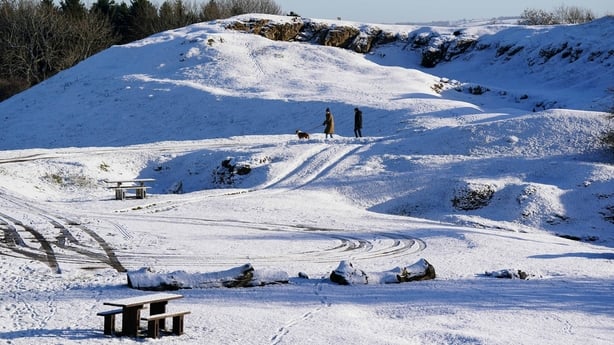 People walk a dog through snow-covered hills