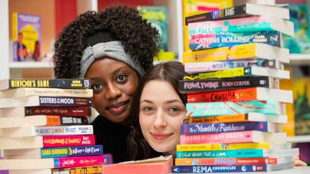 Two people pose for a photo behind two stacks of books