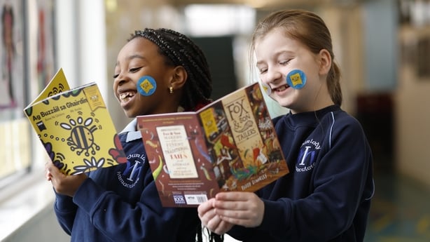 Two girls wearing school uniforms smile as they read books