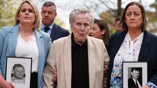 three women are pictured, with two holding black and white photographs of a man