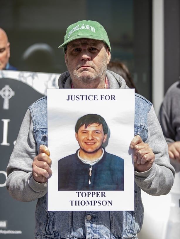 A man holds an image with the words 'justice for topper thompson'