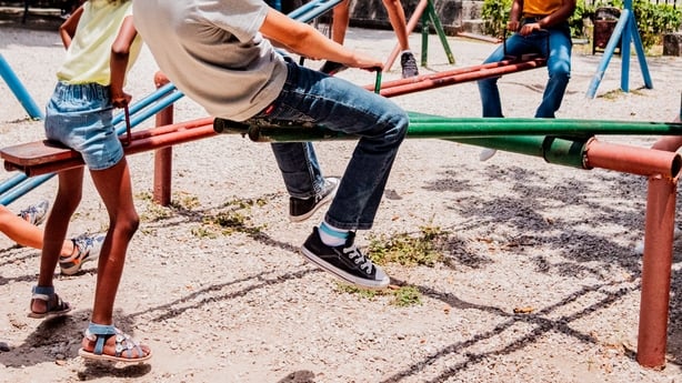 Children are playing on a seesaw at a playground in the sunshine.