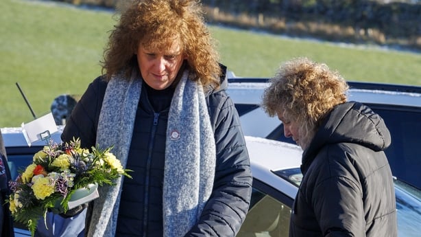 Two middle aged women wearing heavy coats and scarves carry a bouquet of flowers outdoors