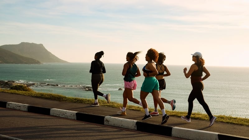 Five young women athletes are running by the sea at sunset, enjoying a healthy lifestyle