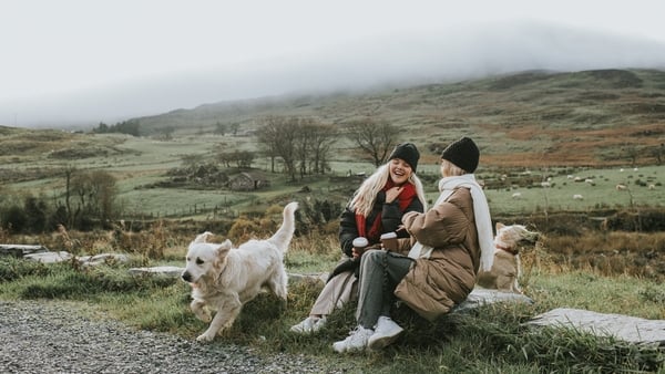 Two young woman in thick coats, hats and scarves with their dog