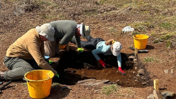 three people work with trowels at an archaeological site
