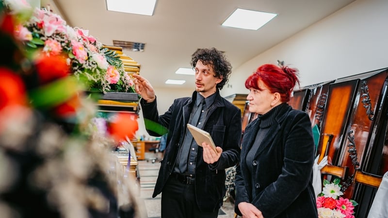 Undertaker showing coffins to a mature widow in funeral parlor.