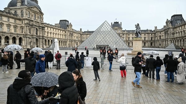 Tourists stand next to barriers blocking the plaza with the Louvre Pyramid in the background