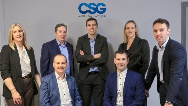 Business men and women pose around a table with the CSG logo in the background