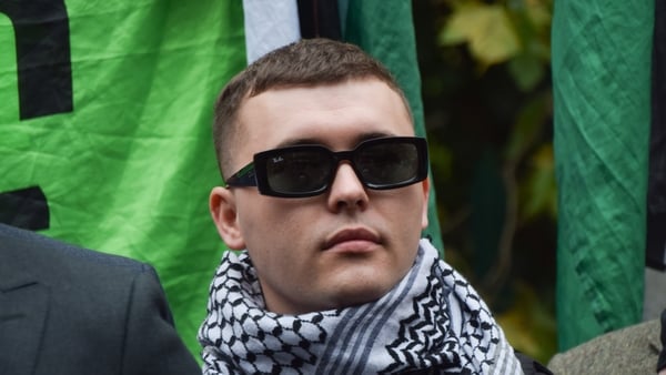A man wearing sunglasses and a scarf with flags in the background