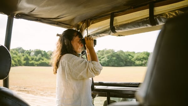 Woman on safari uses binoculars to spot wildlife from a vehicle.