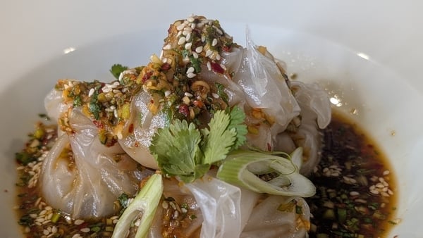 A bowl of rice paper dumplings in a dark sauce, topped with green onions