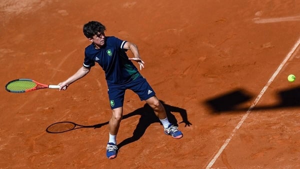 A tennis player wearing blue clothing prepares to hit a tennis ball on clay court