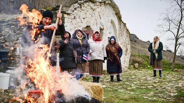 women wearing traditional Moldovan clothes watch a man preparing a slaughtered pig