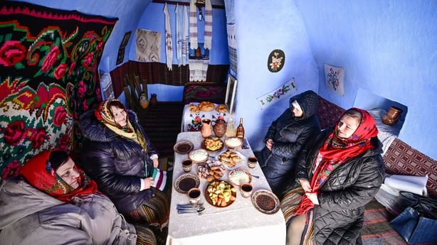 Women wearing traditional Moldovan clothes sit to eat a meal