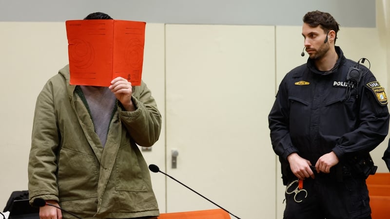 The defendant, partially identified as Farhad N., hides behind a folder as he arrives in the courtroom at the start of his trial