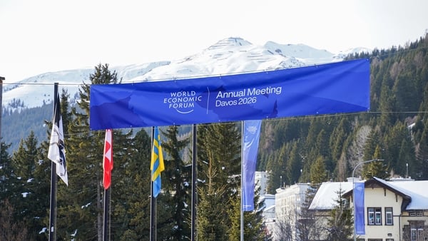 A blue banner with WEF Davos signage draped across flagpoles with snowy mountains in the background