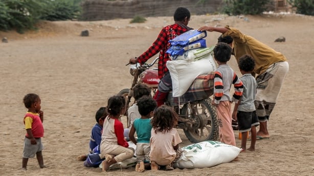 Several children, with their backs to the camera, gather around a motorcycle to receive aid packages.