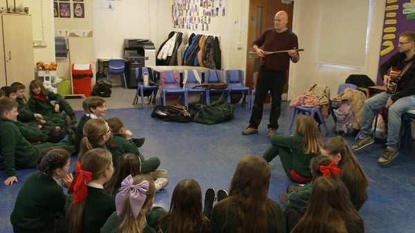 Musicians play traditional Irish music in a classroom with children sitting listening.