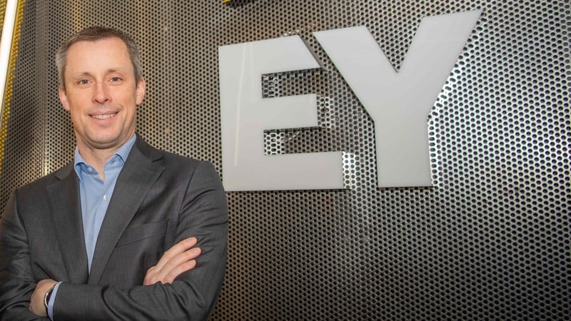 Simon MacAllister standing with arms folded in front of EY sign