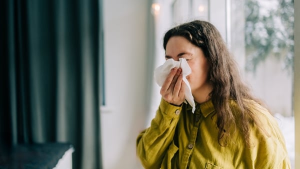 Sick woman blowing her nose with tissue paper at home, suffering from allergy or flu