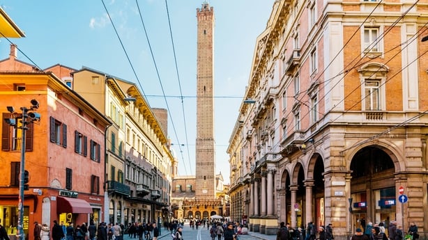 A tower can be seen in the background between two buildings as people cross the street in a city