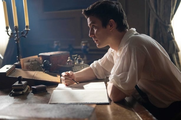 A male character seated at a writing desk in a scene from Bridgerton