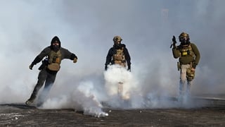 A federal agent kicks a tear gas cannister and others hold weapons after a shooting by ICE agents in Minneapolis