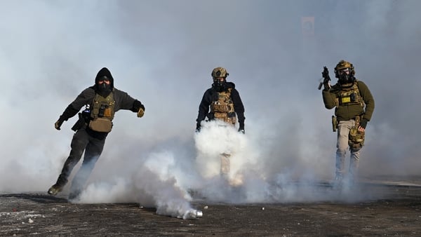 A federal agent kicks a tear gas cannister and others hold weapons after a shooting by ICE agents in Minneapolis