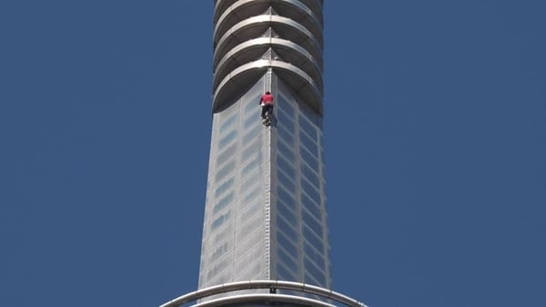 A man wearing a red t shirt climbs a tower block