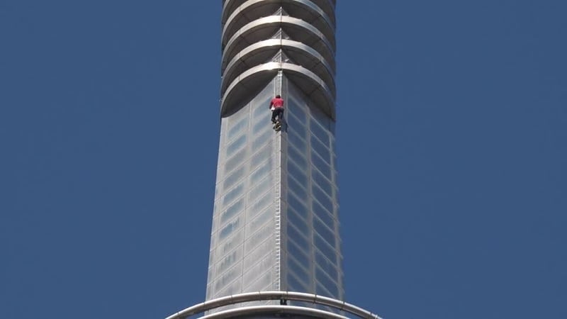 A man wearing a red t shirt climbs a tower block