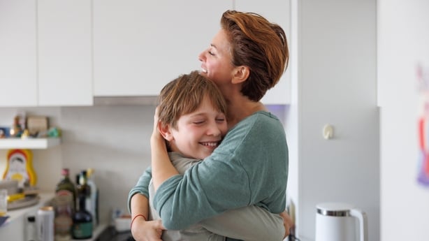Middle-aged woman smiling and embracing lovingly her happy son in the kitchen at home, affection and physical touch