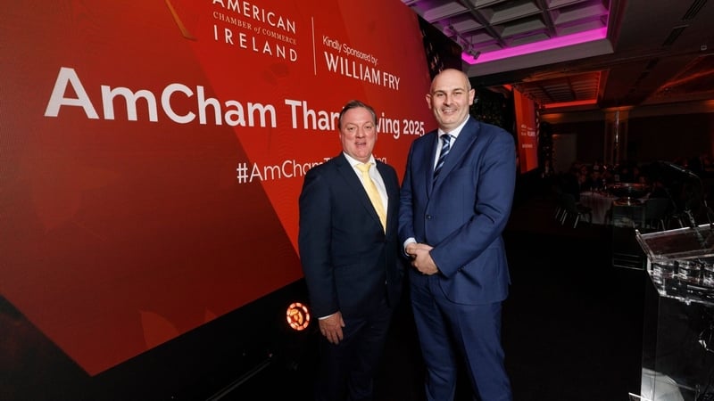 Two business men pose for a photo with American Chamber of Commerce Ireland signage in the background