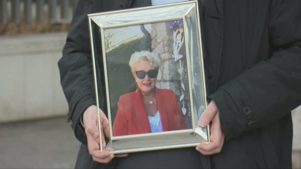 Man holding framed pictured of elderly woman in red blazer and sunglasses