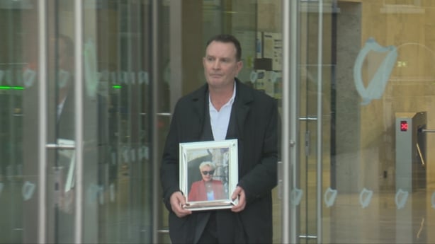 Man holding a framed picture of his wife as he walks out of the CCJ