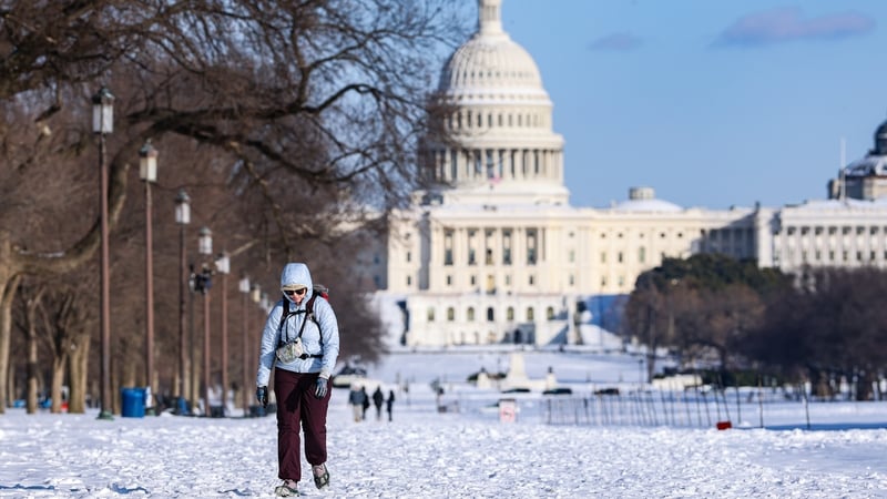 A pedestrian walks through snow in front of the US Capitol