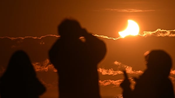People watch a partial solar eclipse at New Brighton, a coastal suburb of Christchurch, on September 22, 2025. A solar eclipse occurs when the moon passes between Earth and the sun, casting a shadow on our planet. The sun appeared as a crescent due to thi