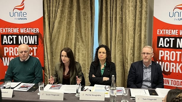 Four people sit at a table with name cards in front and signs in the background