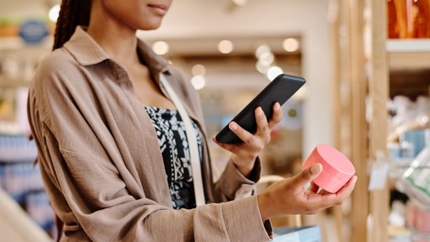 Close-up of young woman taking photo of cream on her smartphone during shopping in the store