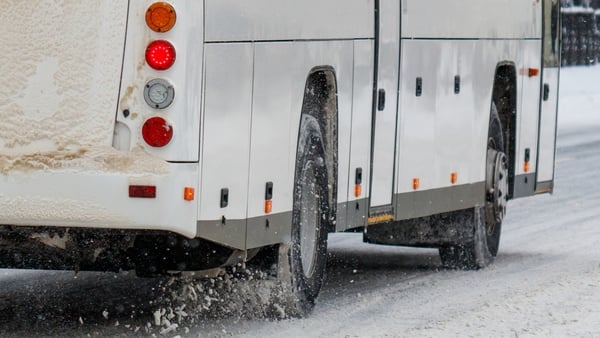 A bus is driving on a snowy road with its headlights on