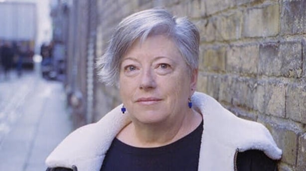 poet Vona Groarke, standing beside brick wall in cityscape