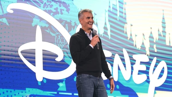 A businessman on a stage with a mic and the Disney logo in the background