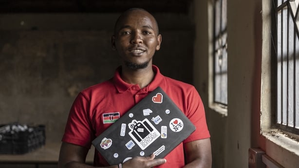 A man wearing a red shirt holds a laptop to his chest