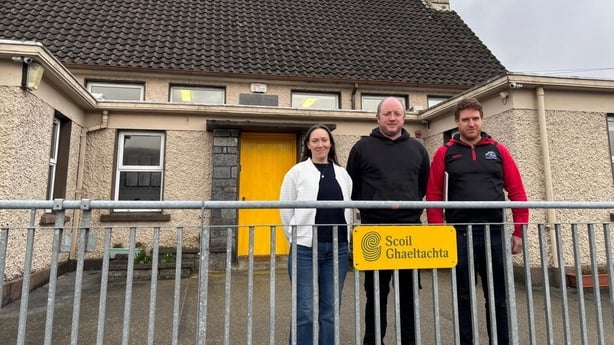 a woman and two men stand outside a small school in rural ireland 