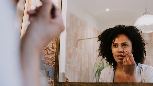 A young woman applies a neutral concealer under her eyes.