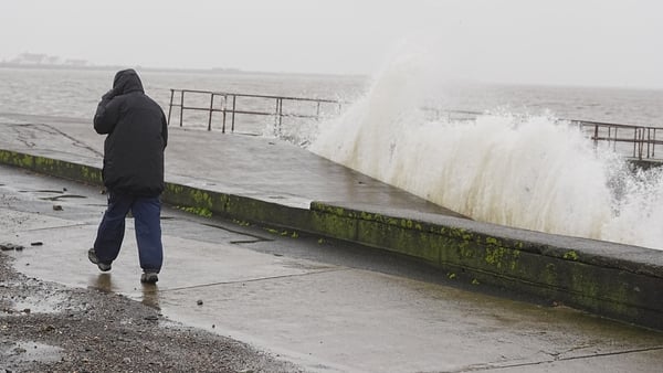 A person walks along the promenade as waves crash against the sea wall prior to high tide in Clontarf, Dublin