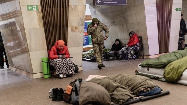 People sit on folding chairs while others sleep on the floor as a man in military uniform walks past in a metro station, in Kyiv, Ukraine on February 7, 2026